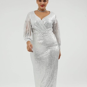 May include: A silver sequined formal gown with a V-neckline and long sleeves. The sleeves have sheer, fringed details. The dress has a fitted bodice and a floor-length skirt. The model is wearing a silver choker necklace and silver heels.