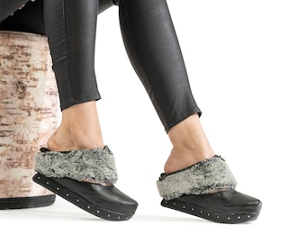 May include: Black leather platform slippers with a gray faux fur trim around the ankle. The slippers have a platform sole with small metal studs.