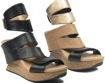 May include: Two pairs of women's wedge sandals. One pair is black leather with a cork wedge sole. The other pair is tan leather with a gold leather strap and a cork wedge sole.