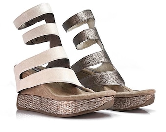 May include: A pair of women's sandals with a woven platform sole. One sandal is white and the other is silver. Both sandals have multiple straps that wrap around the ankle.