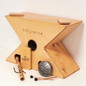 May include: A light-colored wooden musical instrument with an X-shaped design. The instrument has a round hole and includes a flute, a small drum, and drumsticks. The word "buyverse" is printed on the side.