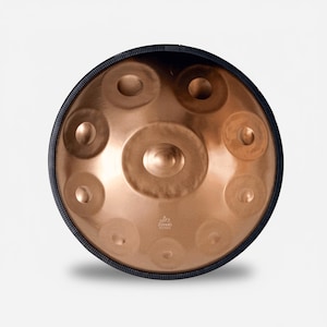 May include: A copper-colored handpan drum with a smooth, metallic finish and a black rim. The instrument features a central dome surrounded by eight circular tone fields arranged in a ring. The text "Zenido Sounds" is printed near the bottom.