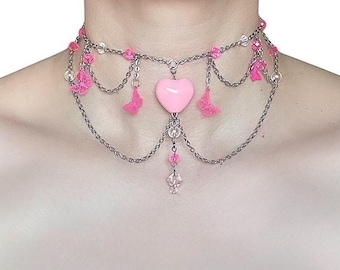 Peut inclure: Un collier ras de cou en chaîne argentée avec un pendentif en forme de cœur rose et des accents de fleurs roses.