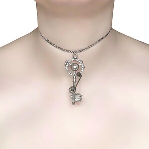 May include: Silver steampunk key pendant necklace. The pendant has intricate gear and cog details, with a circular design at the top and a key-like structure below. The necklace is worn around the neck.