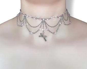 May include: A silver-toned choker necklace with a layered design. The necklace features strands of delicate chains and iridescent beads. A small cross pendant hangs from the center, adding a touch of religious symbolism to the jewelry.