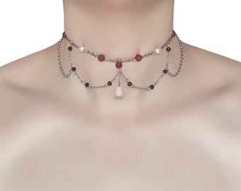 May include: A silver-toned choker necklace with two tiers of chain. The top tier features red beads and a single pearl. The lower tier has red beads and a small pink flower pendant. A delicate and elegant piece of jewelry.