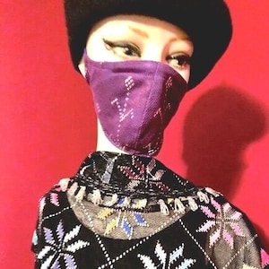 May include: A mannequin wearing a black and white patterned sweater with a purple face mask with a geometric design. The mannequin is wearing a black beret.