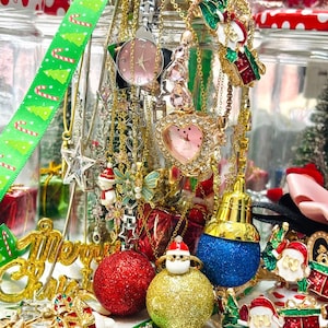 May include: A display of Christmas jewellery and decorations, including necklaces, earrings, and baubles. The image showcases gold, red, green, and blue colours, with glittery and festive details. A green ribbon with Christmas trees is also visible, adding to the holiday theme.