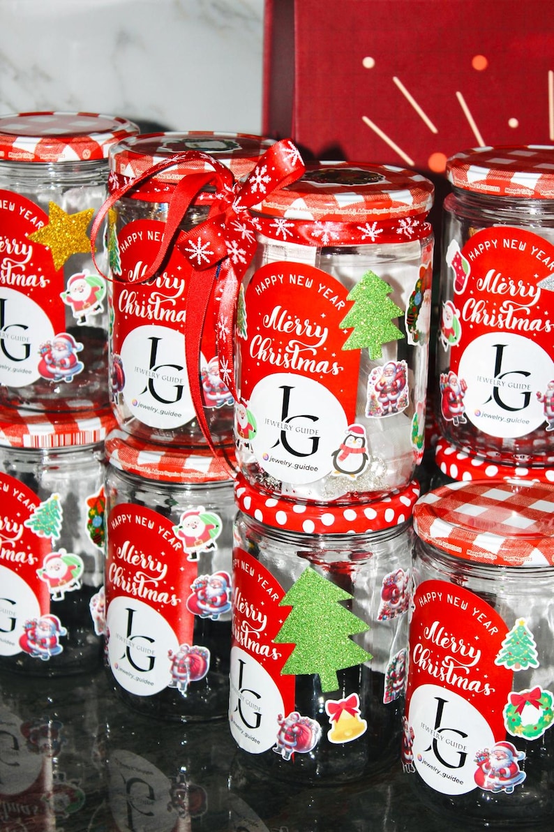 May include: A collection of glass jars with red and white chequered lids, decorated for Christmas. Each jar features a red label with "Merry Christmas" and festive stickers. Some jars are adorned with red ribbons and snowflakes, creating a festive display.