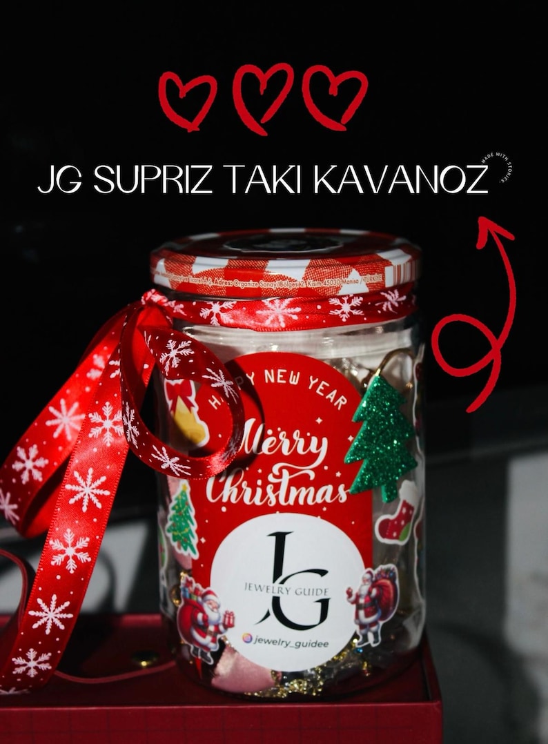May include: A glass jar with a red and white checkered lid, adorned with a red ribbon and a Christmas-themed label. The label says "Merry Christmas" and features a Christmas tree and Santa Claus illustrations. The jar also has the text "JG SUPRIZ TAKI KAVANOZ".