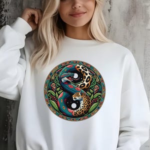 May include: White sweatshirt featuring a circular design with a snake and leopard in a yin-yang composition. The design incorporates vibrant colors like blue, green, and orange, with a detailed border. The sweatshirt is a casual style.