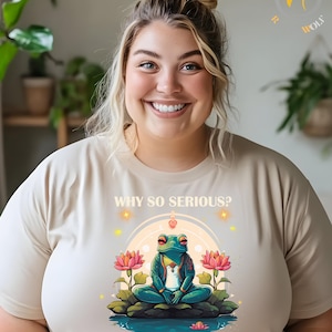 May include: A beige t-shirt with a graphic of a green frog meditating on a lotus flower. The text "WHY SO SERIOUS?" is above the frog and "#bufoalvarius" is below the frog. The word "SAND" is in the bottom right corner of the image.