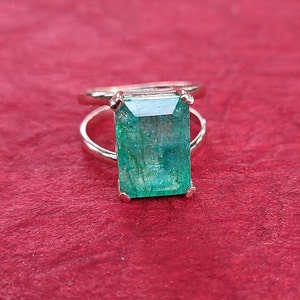 May include: A silver ring featuring a large, emerald green gemstone. The gemstone is cut in a rectangular shape with bevelled edges.