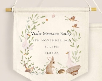 May include: A personalized nursery banner with a watercolor design. The banner features the name "Violet Montana Bailey", date, time, and weight. The design includes a wreath of leaves, birds, a rabbit, a goose, a hedgehog, and a butterfly. The banner is 7 pounds 2 ounces.