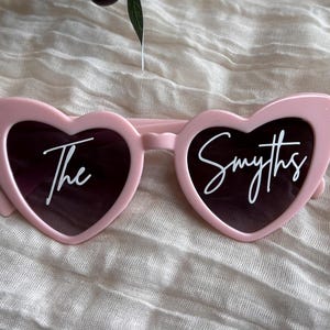 May include: Pink heart-shaped sunglasses with the text "The Smyths" printed in white on the lenses.