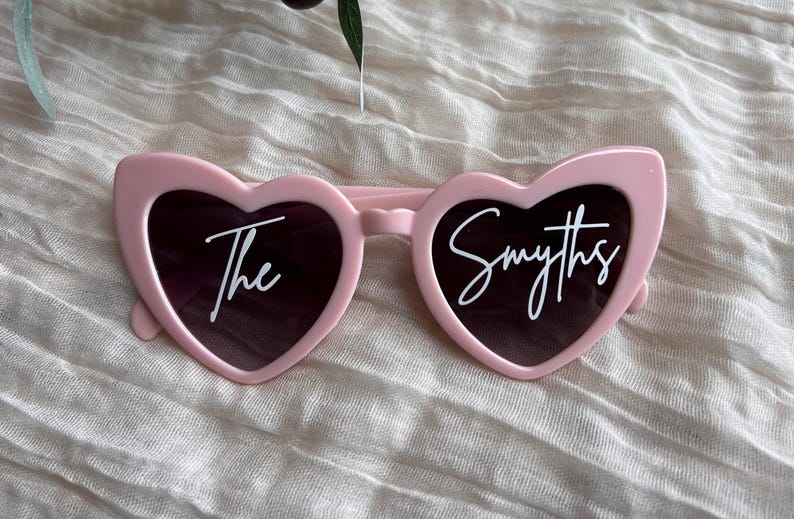 May include: Pink heart-shaped sunglasses with the text "The Smyths" printed in white on the lenses.
