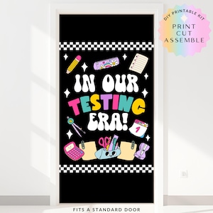 May include: Black door cover with the text "IN OUR TESTING ERA!" and school-themed illustrations. Includes a pencil, calculator, and scissors. The top and bottom have a black and white checkered pattern. The text "FITS A STANDARD DOOR" is at the bottom.