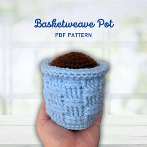 May include: A light blue crocheted basketweave pot filled with brown material. The pot is held in a hand. Text above the pot reads "Basketweave Pot PDF Pattern". The pot has a textured, woven appearance.