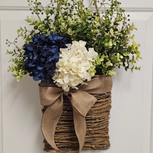 May include: A woven wicker wreath with a burlap bow and blue and white hydrangea flowers.