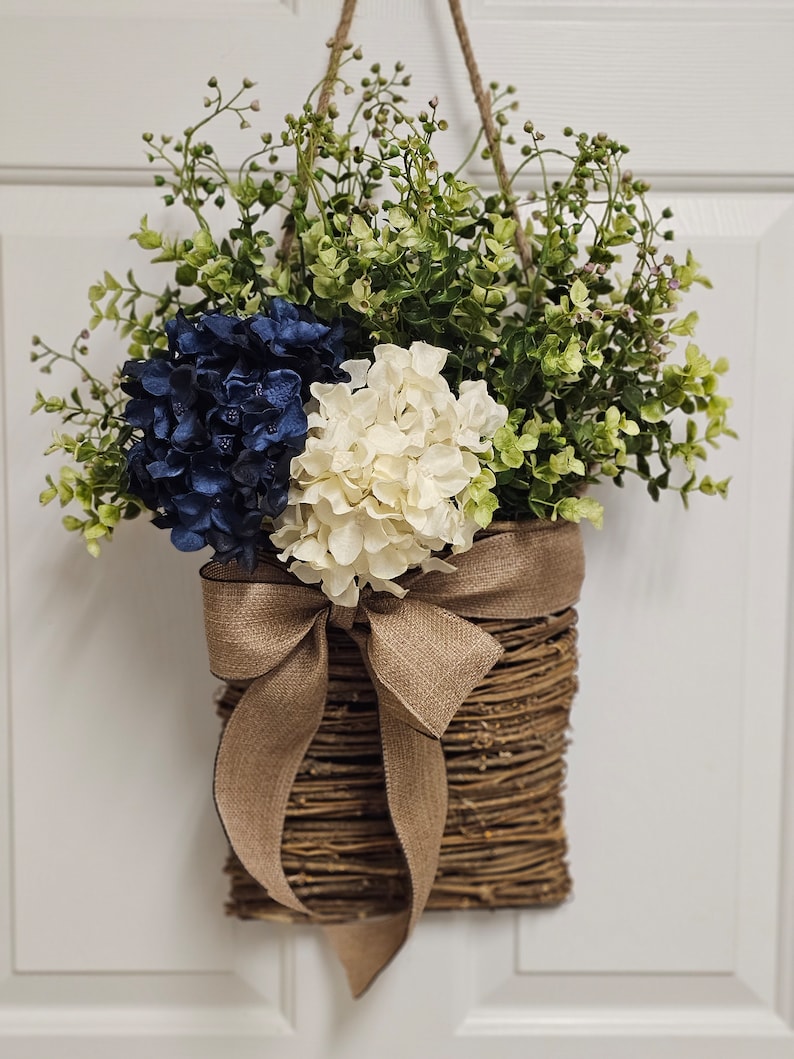 May include: A woven wicker wreath with a burlap bow and blue and white hydrangea flowers.