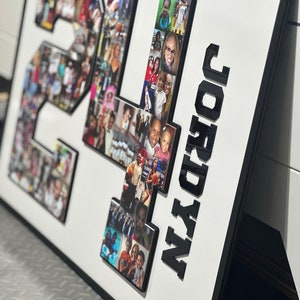 May include: A white framed photo collage with a black background. The collage features a large number "24" made of photos and the name "JORDYN" in black letters. The photos are of a family and are arranged in a grid pattern.