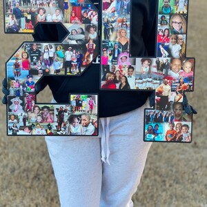 May include: Two large black numbers, 21, are decorated with a collage of photos. The numbers are held by a person wearing a black hoodie and grey sweatpants.