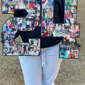 May include: Two large black numbers, 21, are decorated with a collage of photos. The numbers are held by a person wearing a black hoodie and grey sweatpants.