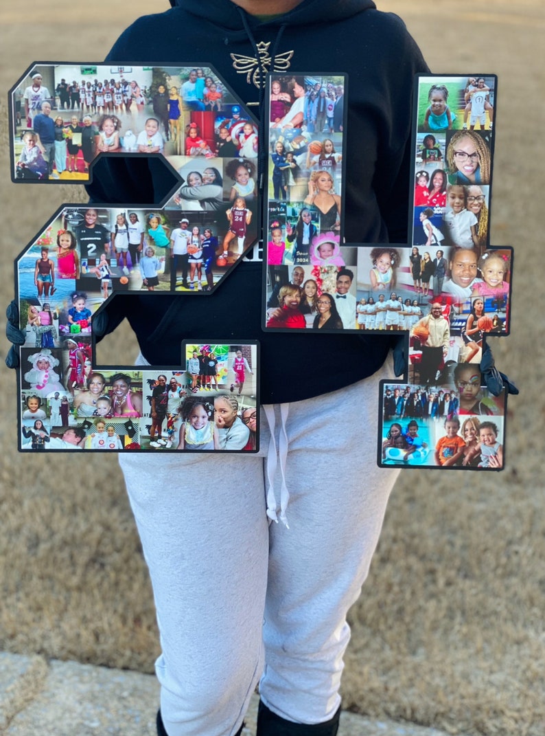 May include: Two large black numbers, 21, are decorated with a collage of photos. The numbers are held by a person wearing a black hoodie and grey sweatpants.