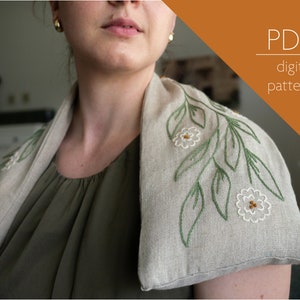 Può includere: Un copri-collo in lino beige con foglie ricamate in verde e fiori ricamati in bianco. Il copri-collo è indossato da una persona con una camicia verde. Il testo "PDF digital pattern" è nell'angolo in alto a destra dell'immagine.