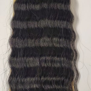 May include: Black and dark brown wavy hair extensions. The extensions are bundled at the top with gold-colored wire. The hair has a natural wave pattern and a blend of colors.