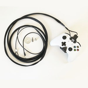 May include: A white wireless video game controller with black buttons and a black cord. The cord is wrapped in black fabric and is connected to the controller.