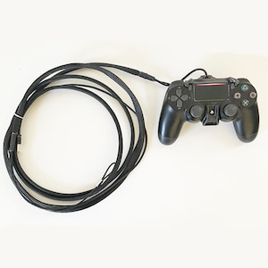 May include: A black PlayStation 4 controller with a black braided cable. The cable is coiled up and the controller is lying on a white surface.