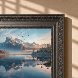 May include: A framed landscape print featuring a serene lake reflecting snow-capped mountains under a clear sky. A flock of birds flies across the horizon above the water. The artwork is encased in a dark, ornate, textured wooden frame with carvings.