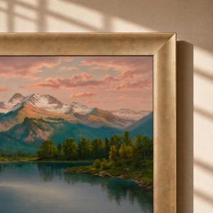 May include: A framed landscape painting depicting a serene lake in the foreground with a dense forest of green trees along the shoreline, leading to snow-capped mountains under a soft pink and orange sunset sky with scattered clouds.