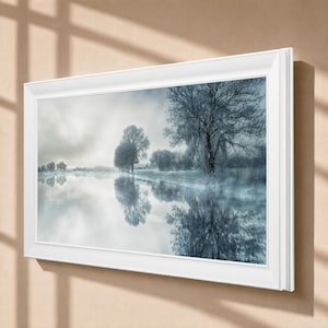 May include: A rectangular wall art piece featuring a landscape photograph of trees reflected in a calm body of water under a cloudy sky. The image is encased in a thick, white, beveled frame, displaying a cool-toned, monochromatic winter scene.