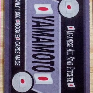 May include: A baseball card with a dark purple border features the name "YAMAMOTO" in large white letters. The card includes Japanese flag graphics and text that reads "Japanese All Star Pitcher" and "Only 1,000 Rookie Cards Made."