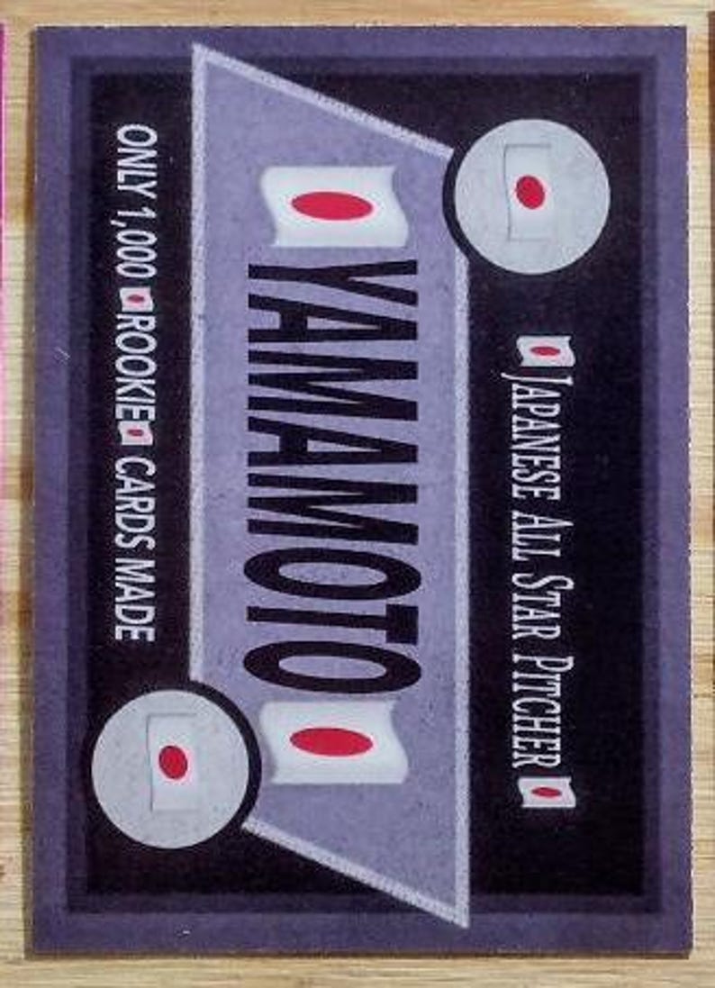 May include: A baseball card with a dark purple border features the name "YAMAMOTO" in large white letters. The card includes Japanese flag graphics and text that reads "Japanese All Star Pitcher" and "Only 1,000 Rookie Cards Made."