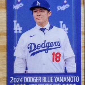 May include: A baseball card featuring a man in a blue Dodgers baseball cap and jersey with the number 18. The card has the text "2024 DODGER BLUE YAMAMOTO" and "JAPAN CY YOUNG AWARD WINNER".