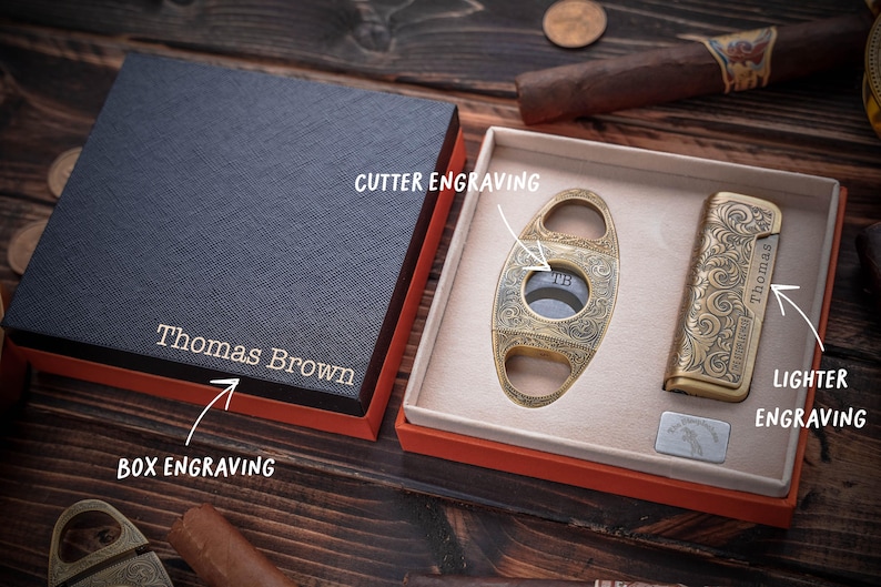 Peut inclure: Un coffret cadeau noir avec le nom Thomas Brown grav&eacute; sur le couvercle, contenant un coupe-cigare dor&eacute; avec la gravure TB et un briquet dor&eacute; avec la gravure Thomas, tous deux orn&eacute;s de motifs &agrave; volutes complexes sur leurs surfaces.