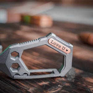 May include: A grey multi-tool with a copper-coloured accent. The tool features a hexagonal opening, a pointed end, and the words "Love U" engraved on the copper accent, along with a heart symbol.