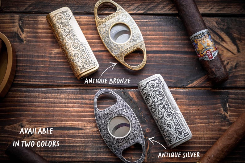 Peut inclure: Deux briquets rectangulaires et deux coupe-cigares ovales avec des gravures &agrave; volutes complexes. Un ensemble est fini en bronze antique et l'autre en argent antique. Les &eacute;tiquettes indiquent : Available in two colors, Antique Bronze, Antique Silver.