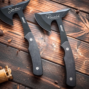 May include: Two black hatchets with wooden handles are displayed on a wooden surface. The hatchets have the names "Jordan" and "Ronald" engraved on them. Other items include a lighter, coins, and a wallet.