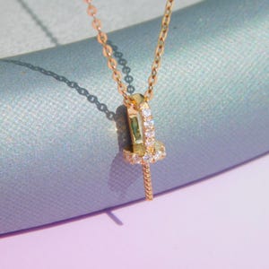 Puede incluir: Un collar de cadena de oro con un pequeño colgante que presenta un círculo de diamantes brillantes. El colgante está unido a una cadena de oro fina.