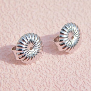 May include: Two silver-toned earring backs featuring a circular, fluted, or scalloped design with a central hole for an earring post. These metallic components have a reflective, polished finish and a distinct radial pattern radiating from the center.