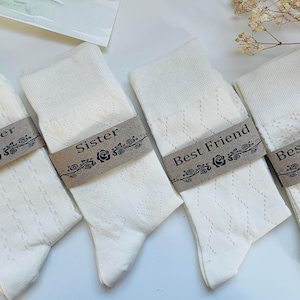 May include: Four pairs of white socks with brown paper tags. The tags have black text that reads "Mother", "Sister", "Best Friend", and "Best Friend".