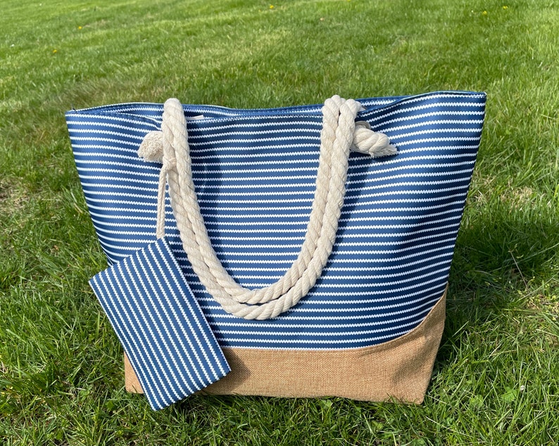 May include: A blue and white striped tote bag with a brown bottom and rope handles. The bag has a matching smaller pouch attached to it.