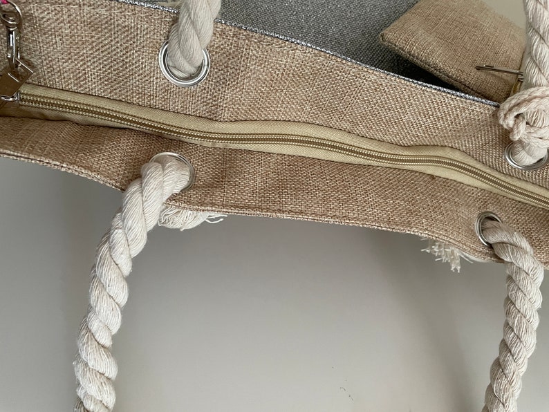 May include: A beige canvas tote bag with a zipper closure and rope handles. The bag has a small pocket on the outside.