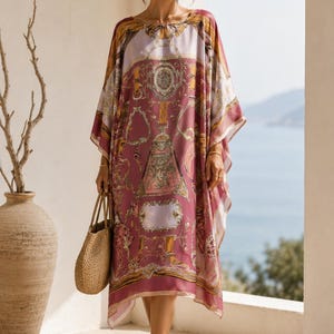 May include: A loose-fitting kaftan dress featuring a mauve and cream color palette with a detailed print of belts, buckles, and ornate circular motifs. The garment has wide, flowing sleeves, a round neckline, and a straight hemline that falls below the knee.