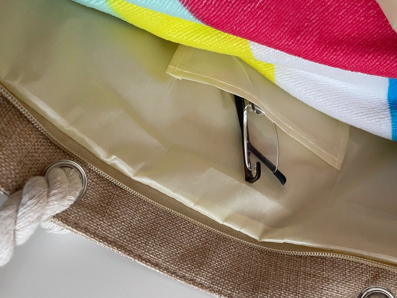 May include: A beige canvas tote bag with a zipper closure and a rope handle. The bag has a light beige lining with a zippered pocket inside. A pair of black glasses is inside the pocket.