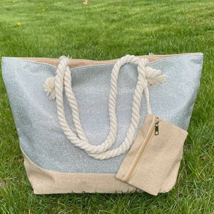 May include: A silver glitter tote bag with a natural canvas bottom and rope handles. The bag has a small zippered pouch attached to the front.